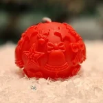 Handmade red soy wax candle in a sphere shape with Christmas motifs such as stars, bells and bows