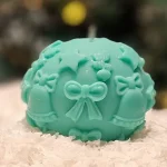 Handmade turquoise soy wax candle in a sphere shape with Christmas-themed decorations such as bells, bows and stars