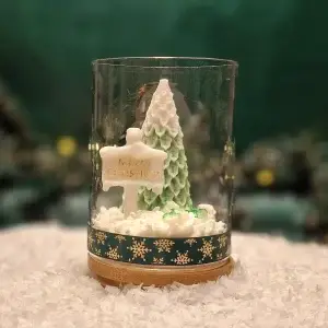 Handgemachte Sojawachskerze in Form eines grünen Weihnachtsbaums und eines Schildes mit der Aufschrift ‘Merry Christmas’, präsentiert in einem Glas mit Holzdeckel und dekorativem Boden