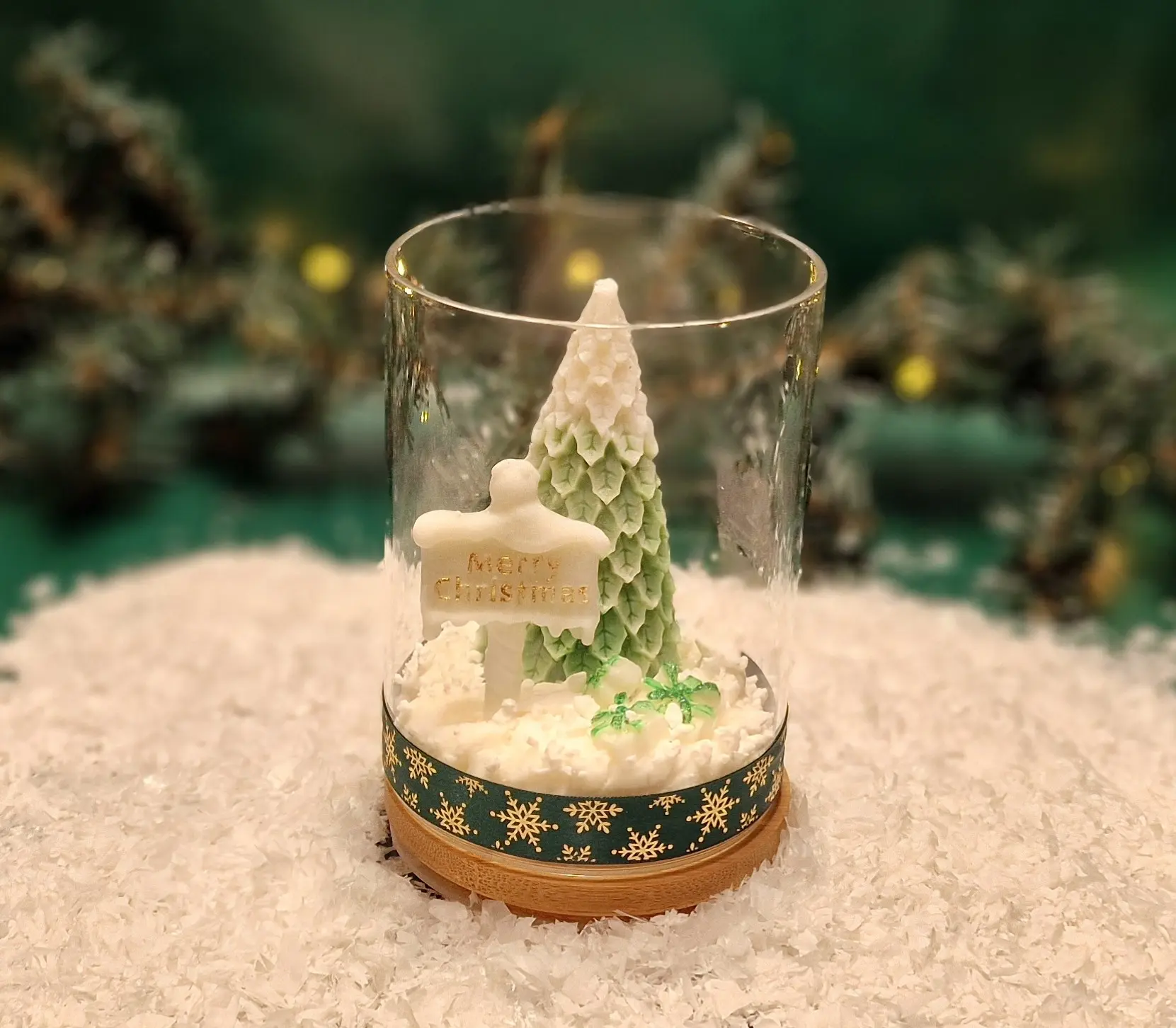 Ręcznie robiona świeca sojowa w kształcie zielonej choinki i tabliczki z napisem ‘Merry Christmas’, umieszczona w szklanym słoiku z drewnianą pokrywką i ozdobną podstawą
