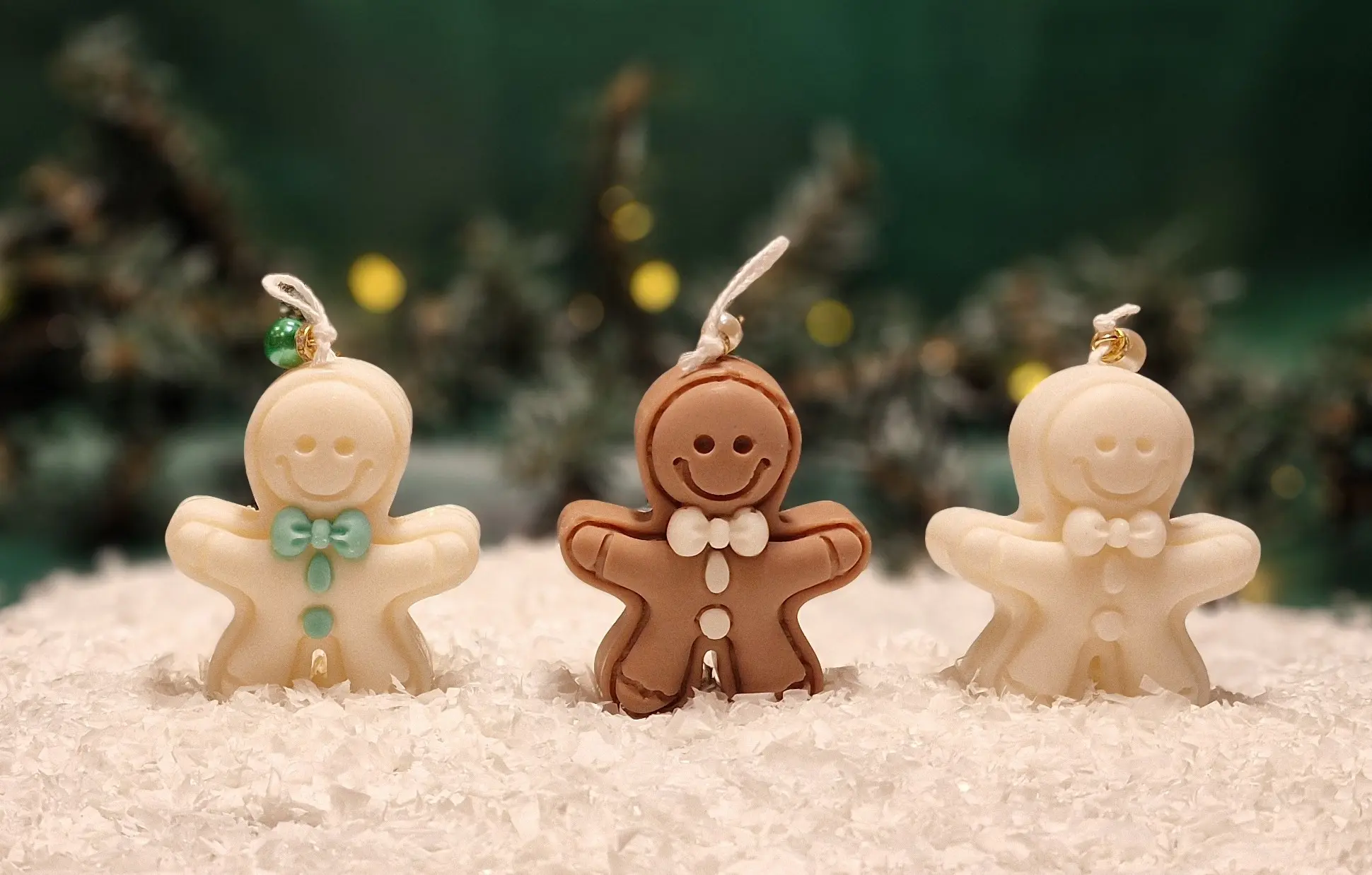 Ręcznie robione świece sojowe w kształcie ludków piernikowych: biały z miętowymi ozdobami, brązowy klasyczny oraz biały z białymi detalami, ustawione na sztucznym śniegu. Ręcznie robione świece sojowe w kształcie ludków piernikowych: biały z miętowymi ozdobami, brązowy klasyczny oraz biały z białymi detalami, ustawione na sztucznym śniegu.