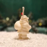 Ręcznie robiona świeca sojowa w kształcie białego Mikołaja, ozdobiona czerwonym koralikiem na sznurku