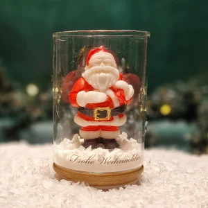 Handgemachte Sojawachskerze in Form eines Weihnachtsmanns in einem Glas mit Holzdeckel und dem Schriftzug ‘Frohe Weihnachten’