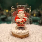 Handgemachte Sojawachskerze in Form eines Weihnachtsmanns in einem Glas mit Holzdeckel und dem Schriftzug ‘Frohe Weihnachten’