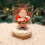 Handgemachte Sojawachskerze in Form eines Weihnachtsmanns in einem Glas mit Holzdeckel und dem Schriftzug ‘Frohe Weihnachten’
