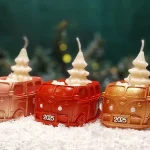 Handgemachte weihnachtliche Sojawachskerzen in Form von 2025-Bussen mit weißen Tannenbäumen als Docht, in Gold-, Rot- und Orangetönen